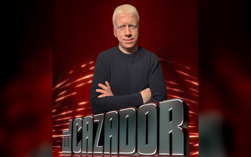 Rubén, de brazos cruzados, sobre el logotipo del concurso El Cazador.