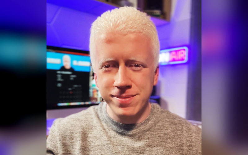 Rubén sonríe en un estudio de radio con luces de neón.